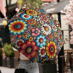 Puede incluir: Un paraguas colorido con un vibrante estampado floral. El paraguas presenta un caleidoscopio de flores en tonos rojos, amarillos, azules y blancos. El diseño se establece sobre un fondo negro, creando un contraste llamativo. El paraguas está abierto, brindando refugio de la lluvia.