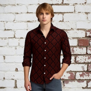 Op de afbeelding: Een bordeauxrood overhemd met zwarte ruitpatroon. Het shirt met lange mouwen heeft een klassieke kraag en witte knopen. Het shirt wordt gedragen met een blauwe jeans.