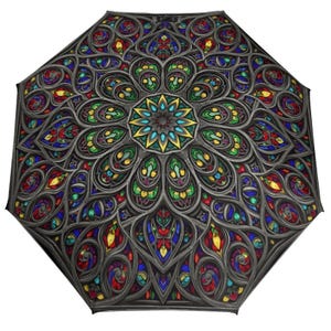 May include: An open umbrella featuring a stained-glass design with a central floral pattern. The umbrella has a dark gray frame and is decorated with colorful glass panels in shades of red, blue, green, and yellow.