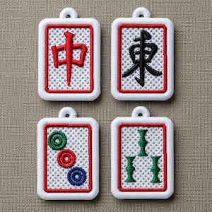May include: Four embroidered Mahjong tile pendants. Each pendant has a white background with a red border and a small loop at the top. The tiles feature Chinese characters and suit symbols in red, black, green, and blue.