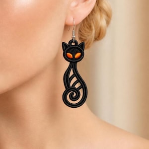 May include: A black embroidered cat-shaped earring featuring a stylized feline silhouette with a curled tail and two vibrant orange eyes. The design is crafted with dense black thread stitching and hangs from a silver-toned metal hook wire.