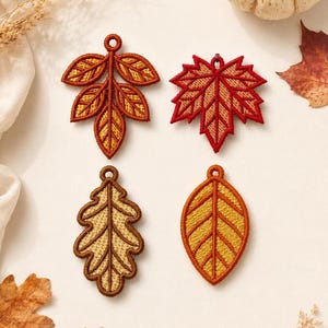 May include: Four embroidered leaf-shaped ornaments featuring a small circular loop at the top. The set includes a compound leaf in orange and yellow, a red maple leaf, a tan oak leaf with brown edges, and an oval yellow leaf with orange borders.