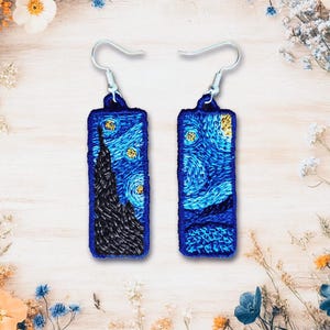 May include: A pair of earrings featuring a blue and yellow embroidered image of Vincent van Gogh's "Starry Night" painting.