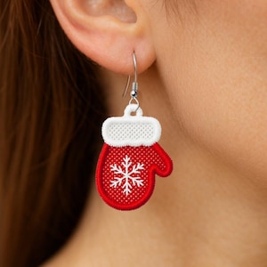 May include: A red and white mitten-shaped earring with a snowflake design. The mitten has a white cuff and a silver-colored hook. The earring is a festive accessory, perfect for the holiday season.