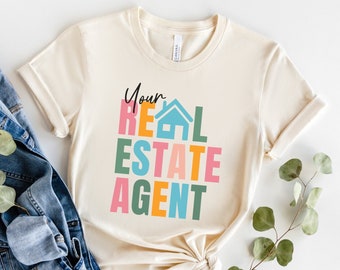 May include: A beige t-shirt with the text "Your Real Estate Agent" in colorful block letters. The letters are in pink, blue, orange, green, and yellow.