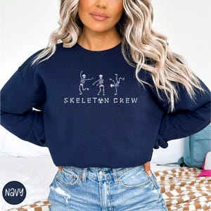 May include: A navy blue sweatshirt with a white graphic of three skeletons dancing. The text "Skeleton Crew" is printed below the skeletons.