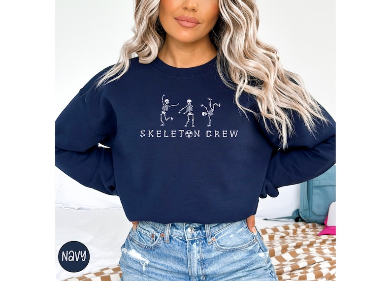 May include: A navy blue sweatshirt with a white graphic of three skeletons dancing. The text "Skeleton Crew" is printed below the skeletons.