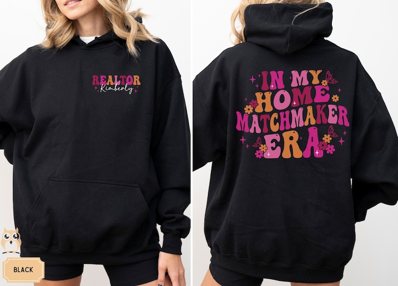 May include: Black hooded sweatshirt with the text "REALTOR Kimberly" on the front and "IN MY HOME MATCHMAKER ERA" with pink and orange lettering and floral accents on the back.