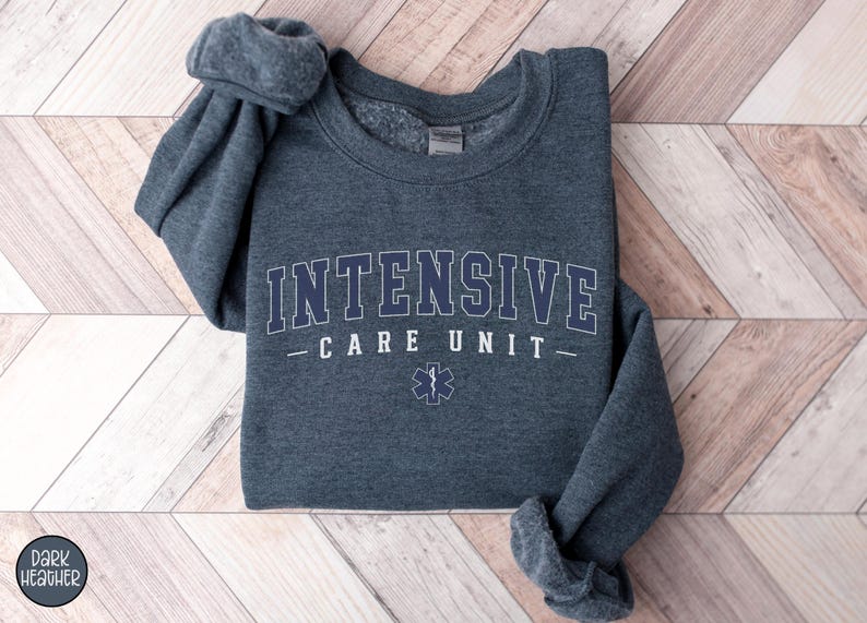 May include: Dark heather grey sweatshirt with the text "INTENSIVE CARE UNIT" in white with a blue outline and a blue medical star symbol.