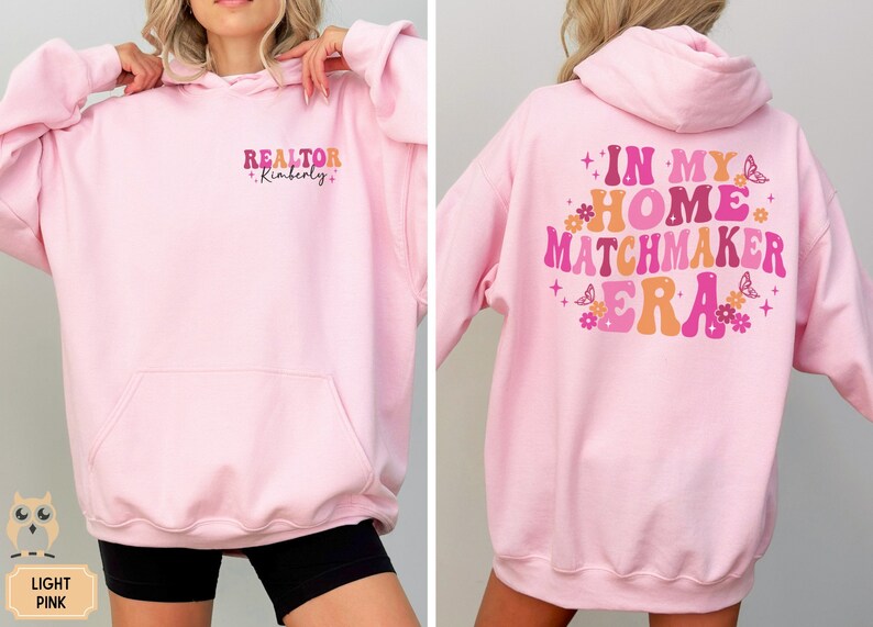 May include: A light pink hoodie with the text "REALTOR Kimberly" on the front and "IN MY HOME MATCHMAKER ERA" on the back. The text is in a retro font with colorful accents.