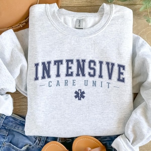 May include: A gray sweatshirt with the text "INTENSIVE CARE UNIT" in blue lettering and a blue medical star symbol.