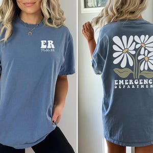 May include: A blue t-shirt with a white daisy design and the text "Emergency Department" on the back. The front of the shirt has the text "ER" and "Maddie RN".