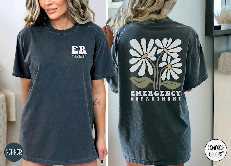May include: A dark gray t-shirt with the text "ER" and "Midwife" on the front and a graphic of three white daisies with green stems and leaves on the back. The text on the back reads "Emergency Department".