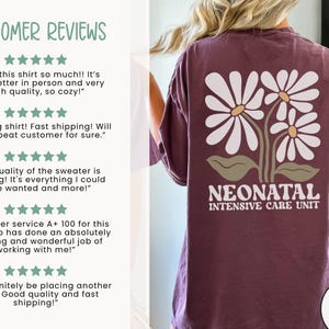 Może przedstawiać: Koszulka w kolorze bordowym z wzorem białych stokrotek i nadrukiem "NEONATAL INTENSIVE CARE UNIT" na plecach. Koszulka jest marki COMFORT COLORS.