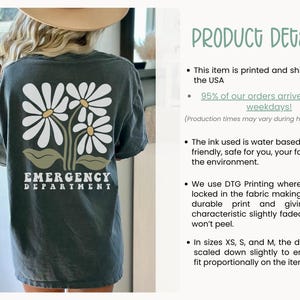 May include: A dark gray t-shirt with a graphic of three white daisies and green leaves. The text "EMERGENCY DEPARTMENT" is printed in white below the daisies.