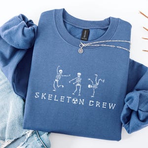 May include: A blue sweatshirt with the text "Skeleton Crew" and a graphic of three skeletons dancing.