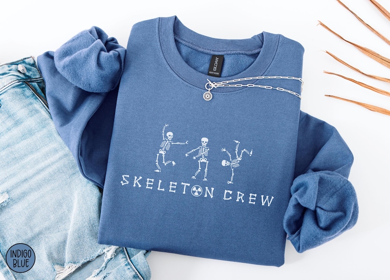 May include: A blue sweatshirt with the text "Skeleton Crew" and a graphic of three skeletons dancing.