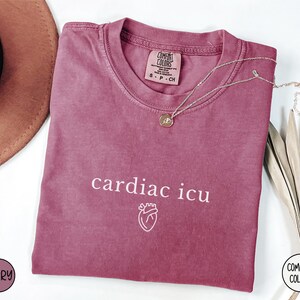 Pu&ograve; includere: Una maglietta color granata con il testo "cardiac icu" e una piccola grafica a forma di cuore stampata in bianco. La maglietta &egrave; realizzata da Comfort Colors.