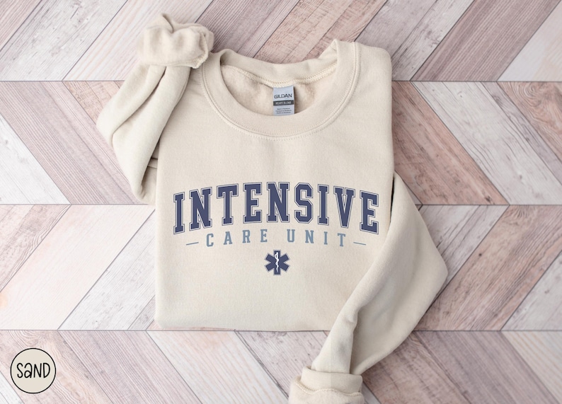 May include: A beige sweatshirt with the text "INTENSIVE CARE UNIT" in blue lettering and a blue star of life symbol.