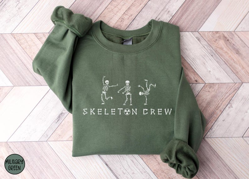May include: A green sweatshirt with a white graphic of three skeletons dancing and the text "Skeleton Crew".