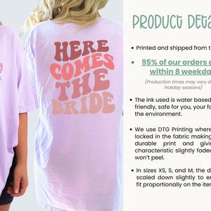 May include: A light purple t-shirt with the text "Here Comes The Bride" in pink, red, and orange retro font. The shirt is printed with a water-based, eco-friendly ink.