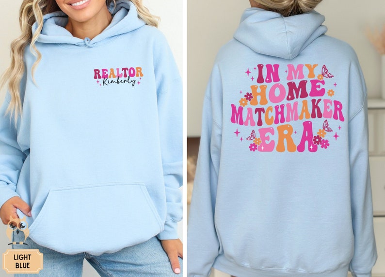May include: Light blue hoodie with the text "REALTOR +Kimberly+" on the front and "IN MY HOME MATCHMAKER ERA" with pink and orange lettering and flowers on the back.