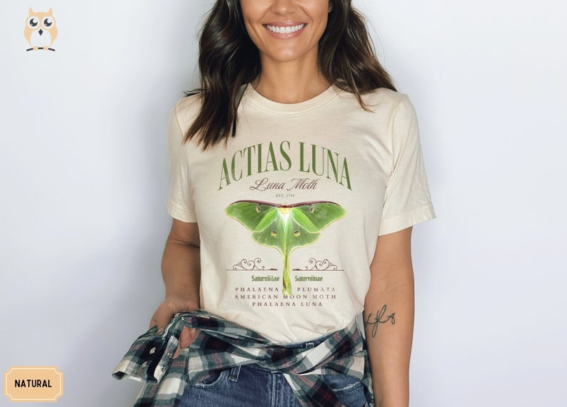 May include: A beige t-shirt with a green luna moth graphic and the text "Actias Luna Luna Moth Est. 1793 Saturniidae Saturniidae Phalana Plumata American Moon Moth Phalana Luna".