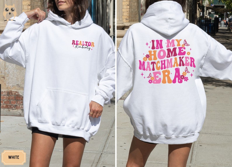 May include: White hooded sweatshirt with the text "REALTOR Kimberly" on the left side and "IN MY HOME MATCHMAKER ERA" with pink and orange lettering and butterfly graphics on the right side.