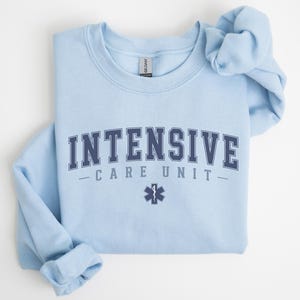 May include: Light blue sweatshirt with the text "INTENSIVE CARE UNIT" in navy blue letters with a navy blue star of life symbol.