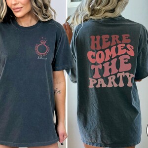 May include: A black t-shirt with a ring and the text "Here Comes The B*tch" on the front and the text "Here Comes The Party" on the back.