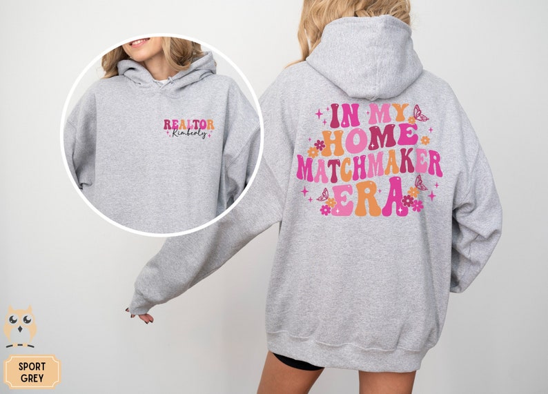 May include: A gray hooded sweatshirt with the text "REALTOR Kimberly" on the front and "IN MY HOME MATCHMAKER ERA" on the back. The text is in a retro font with pink, orange, and yellow colors. The back also features pink flowers and butterflies.