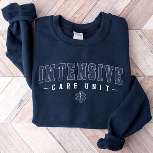 May include: Navy blue sweatshirt with the text "INTENSIVE CARE UNIT" in white lettering and a white medical star with a snake graphic.