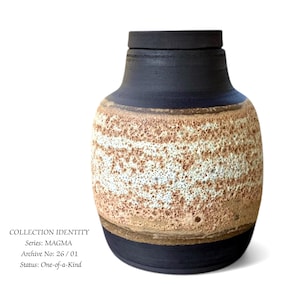 Pode incluir: Um vaso de cerâmica com um design texturizado e em camadas. A parte superior e a base são azul escuro, enquanto a seção intermediária apresenta faixas horizontais brancas, bege e marrons. O vaso tem uma tampa azul escuro correspondente. O texto na imagem diz "COLLECTION IDENTITY".