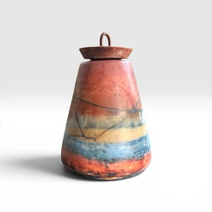 May include: A conical ceramic jar with a lid featuring a small metal loop handle. The surface displays a horizontal gradient of red, orange, yellow, and blue tones with dark, thin, irregular crack-like lines across the exterior body.