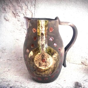 May include: A brown ceramic jug with a handle. The jug has a white and green design with red dots.