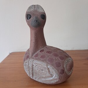 May include: A ceramic bird figurine with a brown and white speckled body and large black eyes. The bird has a long neck and a small beak.