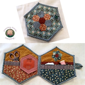 May include: A hexagonal fabric sewing kit with a flower design in shades of brown, red, and green. The kit opens to reveal compartments for needles, thread, scissors, and other sewing supplies. The kit has a fabric handle and is decorated with lace trim.