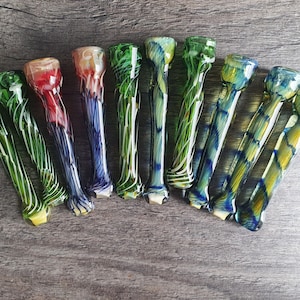 Może przedstawiać: Zestaw dziesięciu kolorowych szklanych fajek do palenia z wirującymi wzorami. Fajki są ułożone w półkole na drewnianej powierzchni.