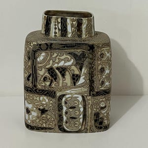 May include: A rectangular ceramic vase with a patterned design. The vase has a square base and a narrower, rectangular opening. The surface is decorated with repeating geometric and stylized fish motifs in shades of brown, black, and white.