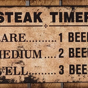 Könnte beinhalten: Ein rustikales braunes Metallschild mit schwarzem Text, auf dem "STEAK TIMER" steht. Das Schild listet den Gargrad eines Steaks und die Anzahl der Biere auf, die man trinken kann, während man auf das Garen wartet: "RARE... 1 BIER", "MEDIUM... 2 BIERE", "WELL... 3 BIERE".