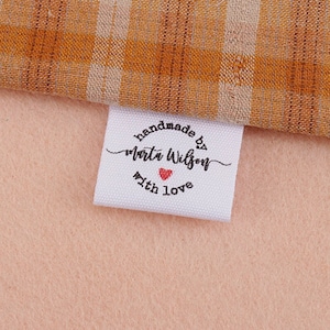 Może przedstawiać: Biała metka z tkaniny z czarnym tekstem, który brzmi "handmade by Marta Wilson with love" i małym czerwonym sercem.