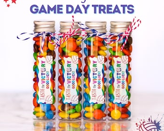 May include: Four clear tubes filled with colorful candies, each with a silver lid and a decorative ribbon. The tubes have labels that read "TASTE the VICTORY GOOD LUCK!" and "Volleyball GAME DAY TREATS" in a volleyball theme.