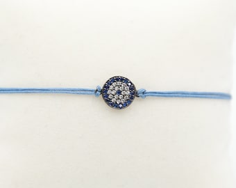 May include: A blue string bracelet with a silver charm featuring a blue and white evil eye design.