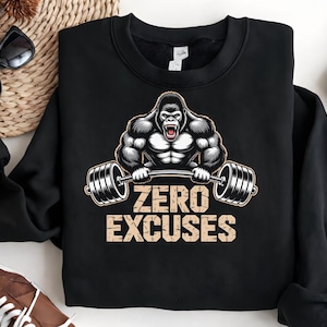 Puede incluir: Sudadera negra con un gorila musculoso levantando una barra. El diseño incluye el texto "ZERO EXCUSES" en una fuente desgastada. La prenda es de cuello redondo y manga larga.