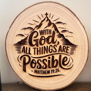 Könnte beinhalten: Ein rundes Holzschild mit einem Berg und den Worten "Mit Gott ist alles möglich - Matthäus 19:26", die in das Holz gebrannt sind.