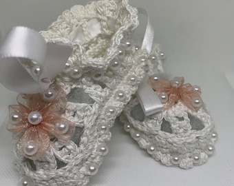May include: White crocheted baby booties with pearl embellishments and a pink satin flower.