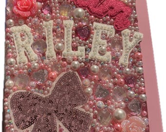 May include: Pink and white iPad case with a sparkly design. The case features a pink bow, the word "Glam" in pink, and the name "Riley" in white.