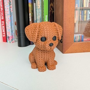 May include: A brown, 3D-printed dog figurine with black eyes and a textured surface. The small dog is sitting on a white surface. The figurine is a decorative item.