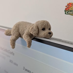 Op de afbeelding: Een klein, beige, getextureerd beeldje van een krulharige puppy die zijn kin en voorpoten over de bovenrand van een computermonitor laat rusten. De puppy heeft donkere ogen en een zwarte neus. Een logo van Little CelticCrafts is zichtbaar.