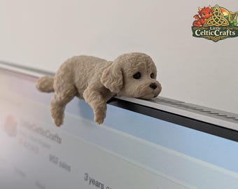 May include: A small, beige, textured figurine of a curly-haired puppy resting its chin and front paws over the top edge of a computer monitor. The puppy has dark eyes and a black nose. A logo for Little CelticCrafts is visible in the corner.